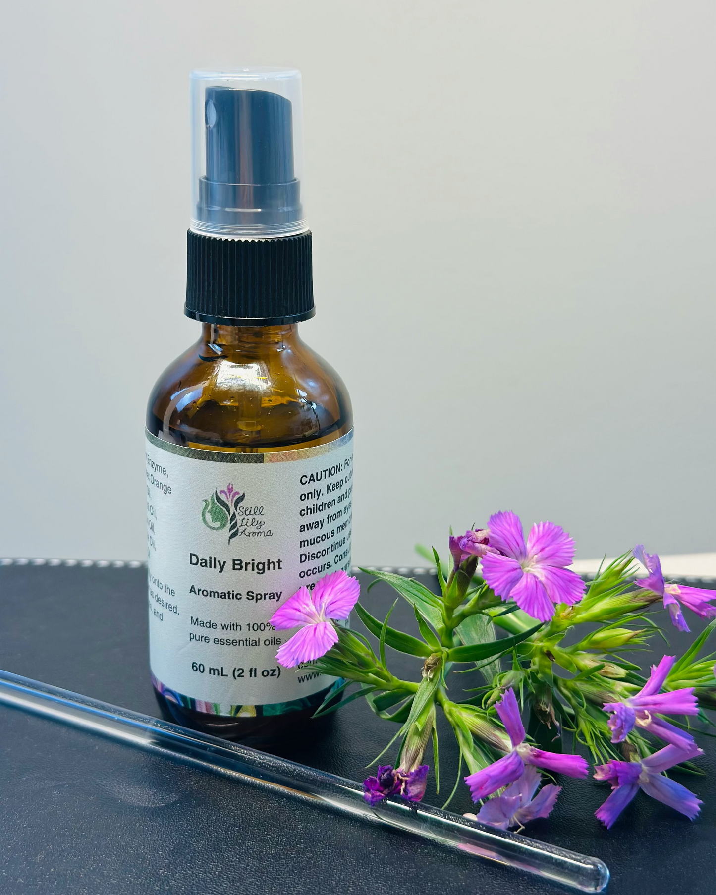 Bottle of 'Daily Bright' aromatic spray with purple flowers on a gray surface
