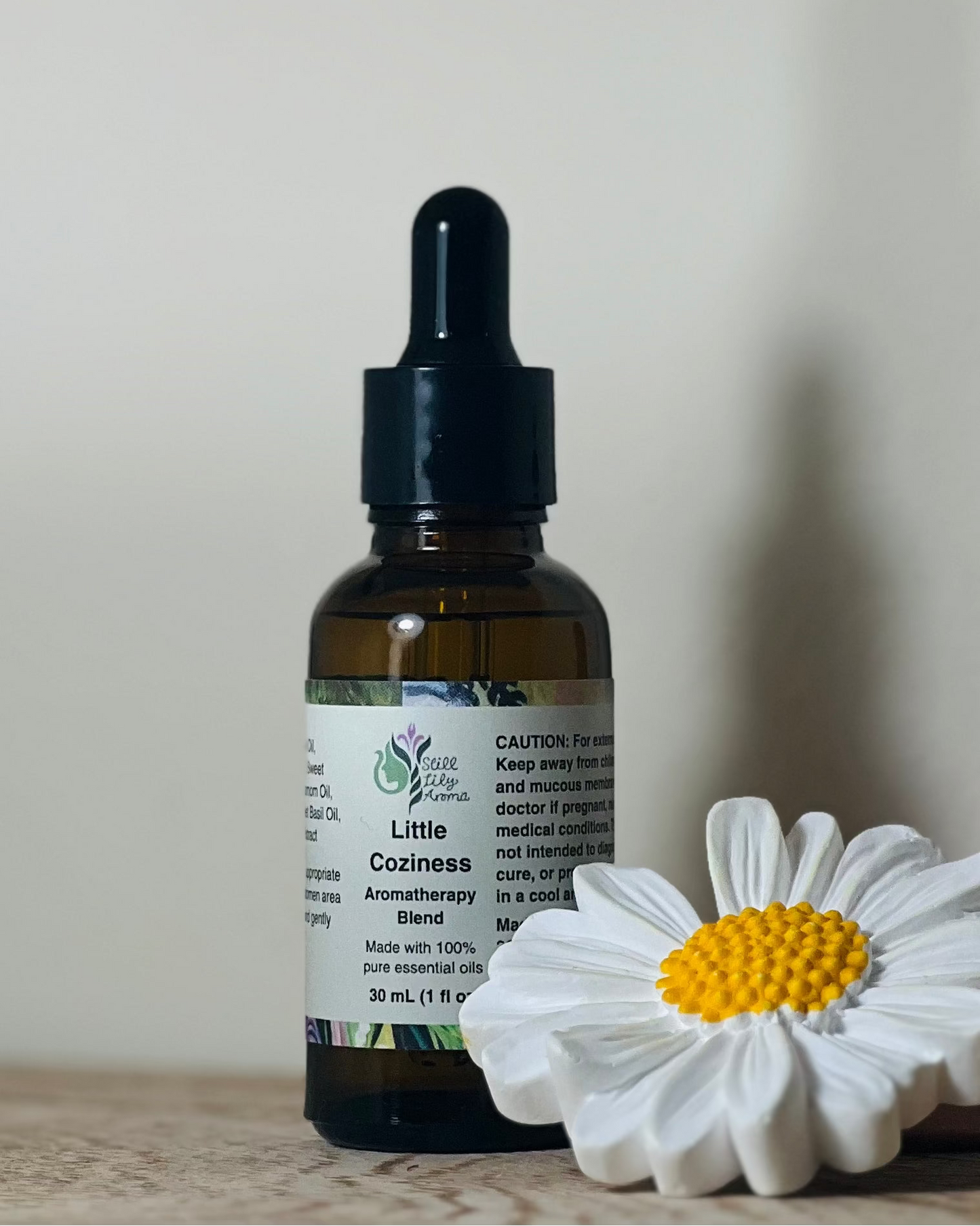 Bottle of Little Coziness Aromatherapy Blend with a white flower on a light background