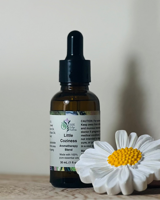 Bottle of Little Coziness Aromatherapy Blend with a white flower on a light background