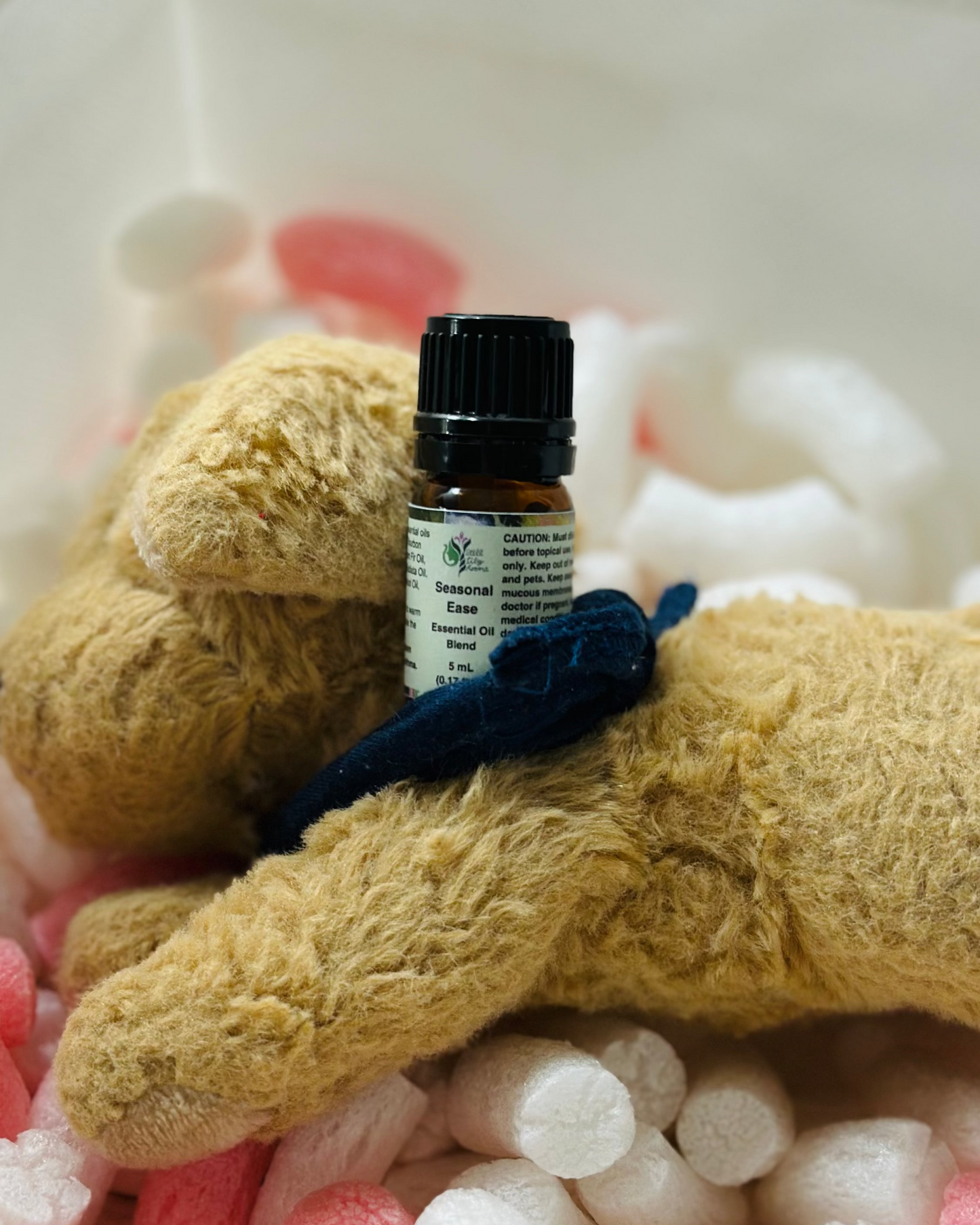 Small bottle of Seasonal Ease essential oil on a plush toy surrounded by colorful cotton balls